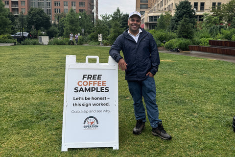 A photo of the founder, Andrew, at the MetPark farmers market in Arlington, VA next to a SipSation sign.